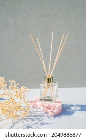 Transparent Bottle Of Aroma Diffuser On A Light Grey Background. Eau De Parfum For Home Presentation On A Podium With Dry Plant And Shadows . Trending Concept In Natural Materials.