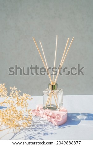 Transparent bottle of aroma diffuser on a light grey background. Eau de parfum for home presentation on a podium with dry plant and shadows . Trending concept in natural materials.