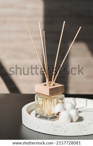 Transparent bottle of aroma diffuser on the terazzo podium on blurred room background. Eau de parfum for home presentation on a podium with cotton flowers. Trending concept in natural materials.