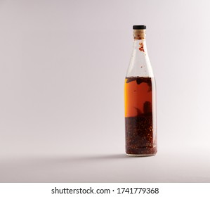 Transparent Bottle Of Homemade Chilli Oil With Pieces Of Dry Chilli, On A White Background