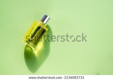Transparent bottle of perfume on a green background. Natural light and shadows. Women's and men's essence concept, flatlay