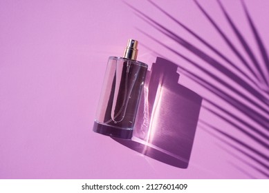 Transparent Bottle Of Perfume On A Lilac Background. Fragrance Presentation With Daylight. Trending Concept In Natural Materials With Palm Shadow. Women's And Men's Essence.