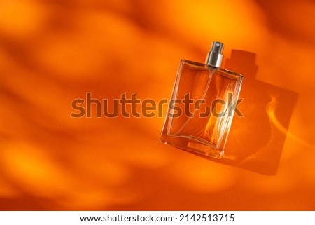 Transparent bottle of perfume on an orange background. Fragrance presentation with daylight. Trending concept with beautiful shadow. Women's essence.