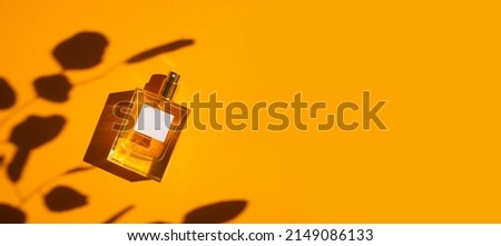 Transparent bottle of perfume on an orange background. Fragrance presentation with daylight. Trending concept in natural materials with plant shadow. Women's and men's essence. Сток-фото © 