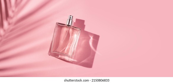 Transparent Bottle Of Perfume On A Pink Background. Fragrance Presentation With Daylight. Trending Concept In Natural Materials Palm Leaves Shadow. Women's And Men's Essence.