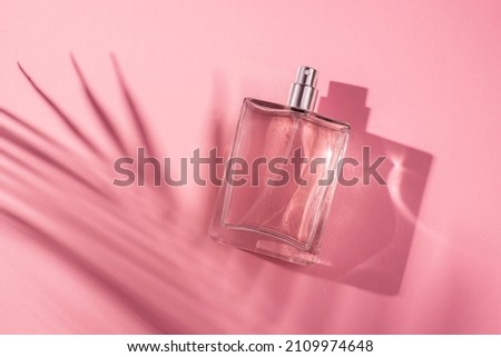 Transparent bottle of perfume on a pink background. Fragrance presentation with daylight. Trending concept in natural materials palm leaves shadow. Women's and men's essence.