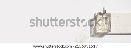 Transparent bottle of perfume on stone plate on a white background. Fragrance presentation with daylight. Trending concept in natural materials with dry plant. Women's and men's essence.