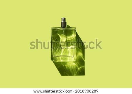 Transparent bottle of perfume with spray on a yellow green background. Beautiful natural light and shadows. Mockup of clear glass fragrance without lid . Cosmetics packaging container top view.