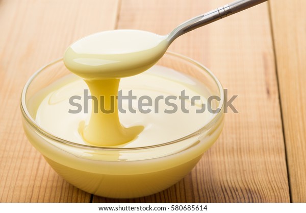 Transparent bowl with condensed milk and teaspoon\
on wooden table