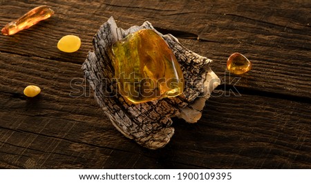 A transparent bright yellow Baltic amber stone lies on a birch bark on a natural dark weathered wooden surface. Ancient amber is healing, protection, powers, magic, good  luck charm. 