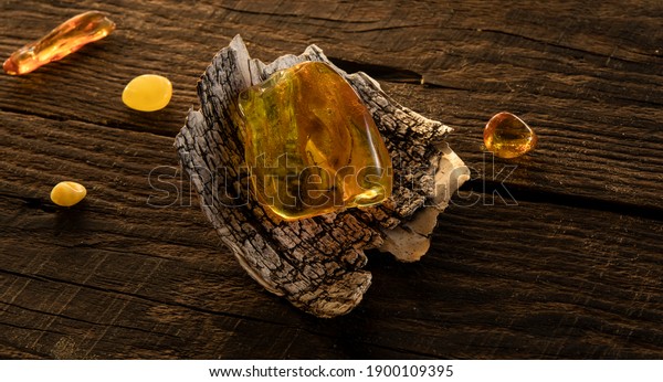 A\
transparent bright yellow Baltic amber stone lies on a birch bark\
on a natural dark weathered wooden surface. Ancient amber is\
healing, protection, powers, magic, good  luck charm.\

