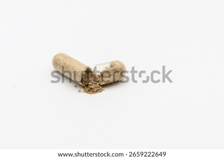 A transparent capsule, split open, with light brown, granular powder spilled onto a pristine white surface, suggesting natural supplements.