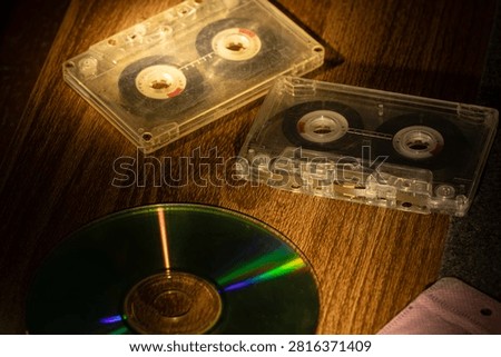 Transparent compact audio cassettes and CD disc on wooden surface with vintage warm lighting