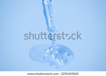 Transparent cosmetic gel flows from an eyedropper directly onto the background in a large blob with bubbles. On a blue background. Hyaluronic acid, toner, toner, gel, cream. Cosmetics.