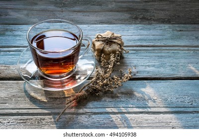 Transparent cup of black tea and dry twig herb, homemade cookies on wooden background. Toned. Top view