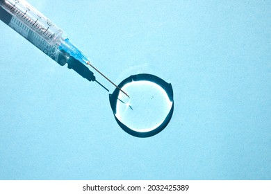 Transparent drop of hyaluronic acid gel and a medical syringe for injections on a blue background. Top view, place for text.