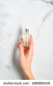 Transparent Dropper Bottle With Serum Lotion Or Essential Oil In Female Hand Over Marble Table. Skin Care Cosmetics Concept.