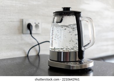 Transparent electric kettle with boiling water on table in the kitchen