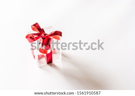 Transparent empty plastic gift box with red ribbon on white background. Festive minimal concept.