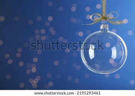 Transparent glass Christmas ball with golden ribbon and bow against blue background. Space for text