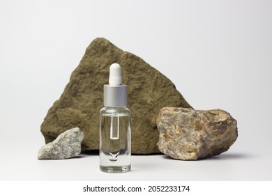 Transparent glass cosmetic bottle with a pipette on a white background with stones. Background for cosmetics. Space for text and labels.