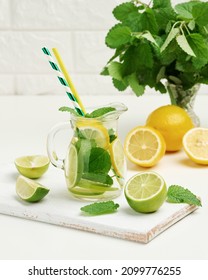 Transparent Glass Decanter With Slices Of Lemon, Lime And Mint Leaves On A White Table, Detox. Behind The Ingredients For The Drink