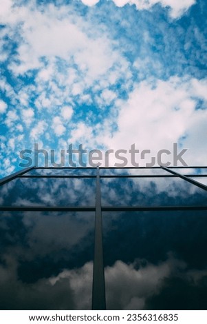 Transparent glass walls of office buildings. A modern office building with a glass facade against a cloudy sky. Glazed building with blue sky. The sky with clouds is reflected in the windows