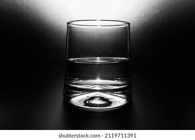 Transparent glass with water half full on black background and spot of light from above