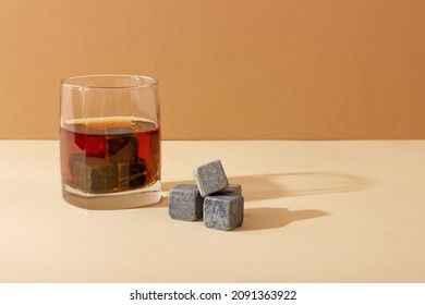 Transparent glass with whiskey on a dark background with bright rays of light. Whiskey stones in a glass glass