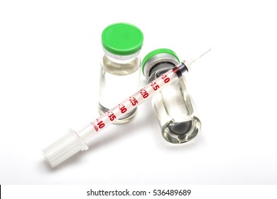 Transparent medical insulin syringe lying on medical bottle with hormone. Another insulin ampule with green cap standing near. White background, shadows. close up image.