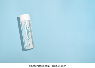 Transparent micellar water in a white plastic bottle on a blue background top view. Makeup cleanser for face skin. Liquid beauty cosmetic for clean fresh skin flat lay