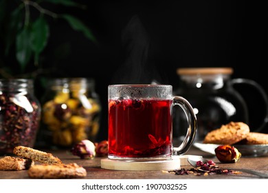 Transparent mug with hot red tea on a dark background, near cookies and tea leaves, horizontal orientation  - Powered by Shutterstock