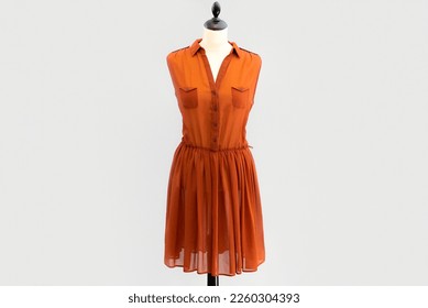 A transparent orange shirtdress dress with buttons hangs on a headless mannequin. isolated by a light gray white background. - Powered by Shutterstock