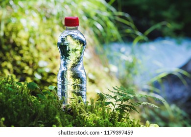 Transparent plastic A bottle of clean water with a red lid stands in the grass and moss on the background of a rugged mountain river. The concept of pure natural drinking water