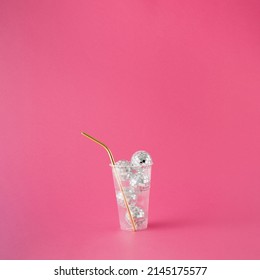 Transparent plastic drinking cup filled with shiny disco balls and golden straw on pink background. - Shutterstock ID 2145175577