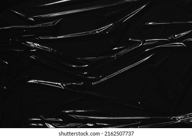 Transparent plastic wrap on black background. Crumpled wrinkled plastic cellophane. Reflecting light and shadow on creases and folds in plastic surface. Texture overlay effect template