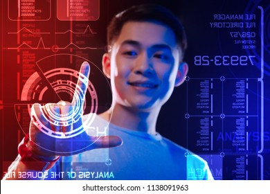 Transparent screen. Cheerful confident programmer smiling and touching the round diagram on the screen while working at the program