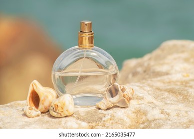 Transparent Spray Bottle Of Women's Perfume With Shells  Close Up On A Stone Against The Backdrop Of The Sea In The Sun. Presentation Of Women's Perfumes In The Sea Environment 