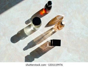 Transparent Unisex Perfume Bottles In Different Sizes And Shapes On Marble Background With Long Shadows.