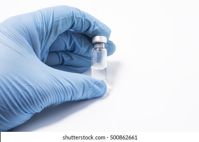 Transparent Vial Or Bottle With The Vaccine Is In The Doctor's Hand, Which Is Dressed In Blue Medical Gloves. The Concept Of Vaccination, Research Or Production Of Vaccines Against Various Diseases