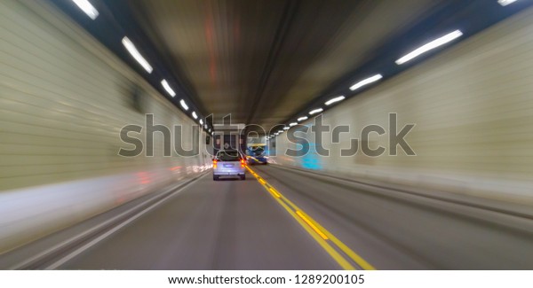 Transport abstract vehicle lights traveling\
through darkened tunnel with long exposure light trails converging\
towards end of\
tunnel.