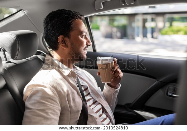transport,\
business and people concept - happy smiling indian man with\
takeaway coffee on back seat in taxi\
car