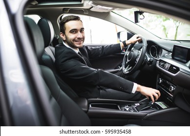 транспорт, деловая поездка, место назначения и концепция людей - близкий образ молодого человека в костюме вождения автомобиля смотреть на камеру