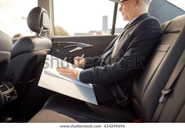 transport, business trip, paperwork and people\
concept - senior businessman signing papers with pen and driving on\
car back seat