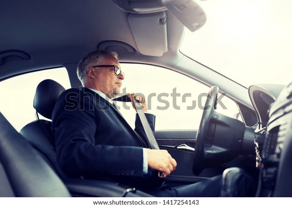 transport,\
business trip, safety and people concept - senior businessman\
fastening seat belt before driving\
car