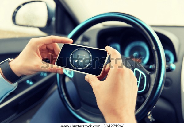 transport, business trip, technology and people\
concept - close up of male hands with musical note icon on\
smartphone screen in\
car