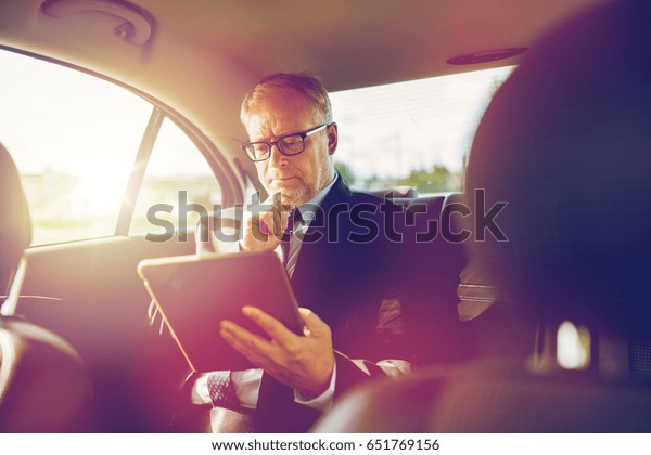 transport, business trip, technology and people\
concept - senior businessman with tablet pc computer driving on car\
back seat