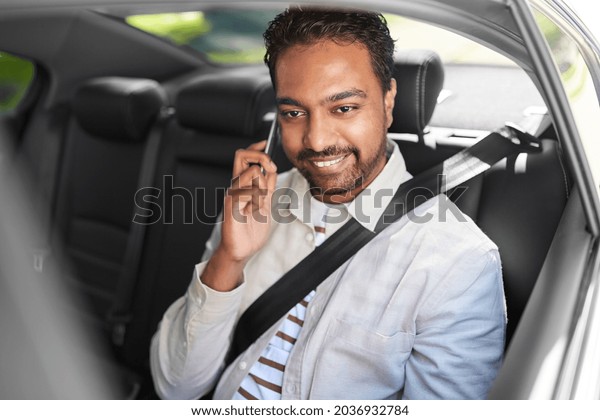 transport, communication and people concept - happy\
smiling indian male passenger or businessman calling on smartphone\
on back seat of taxi\
car