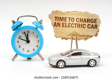 Transport concept. On a white surface there is a blue alarm clock, a car and a sign with the inscription - Time to charge an electric car