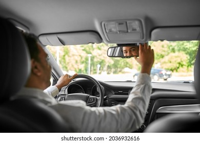 transport, driving and people concept - happy smiling indian man or driver adjusting rearview mirror in car
